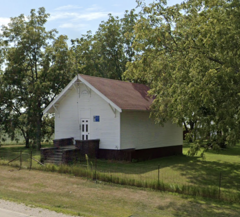 Front and side of the white schoolhouse on a brick base, 2022	