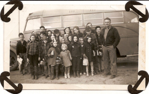 Photo of a group of school children with a bus driver in front of a bus.	