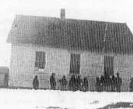 Black and white photo of a schoolhouse with children standing beside it