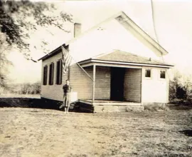Photo of a white schoolhouse with a teacher